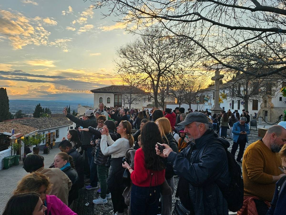 Тълпа при залез на Mirador de San Nicolás в Гранада с панорама към Алхамбра и Сиера Невада. 
